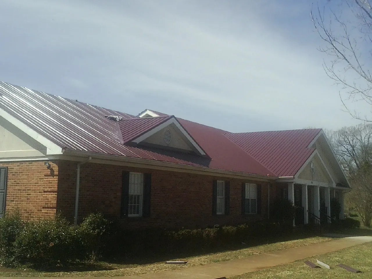 Red metal roof with gabled entries on a long brick building, from a Hail Damage Roof Repair job in Crockett