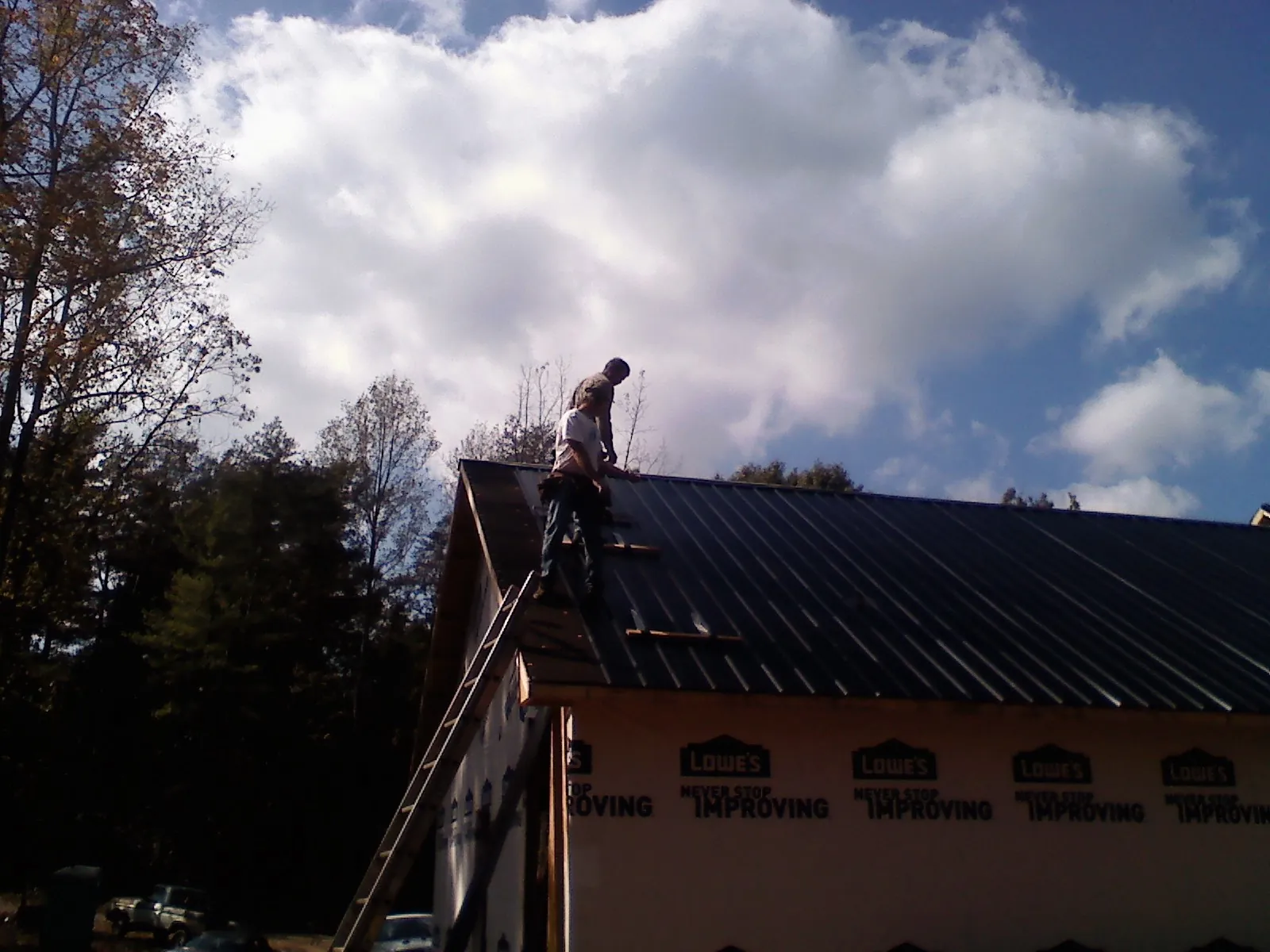 Roofer fastening dark metal panels high against a cloudy sky, from a Roof Inspection job in Crockett