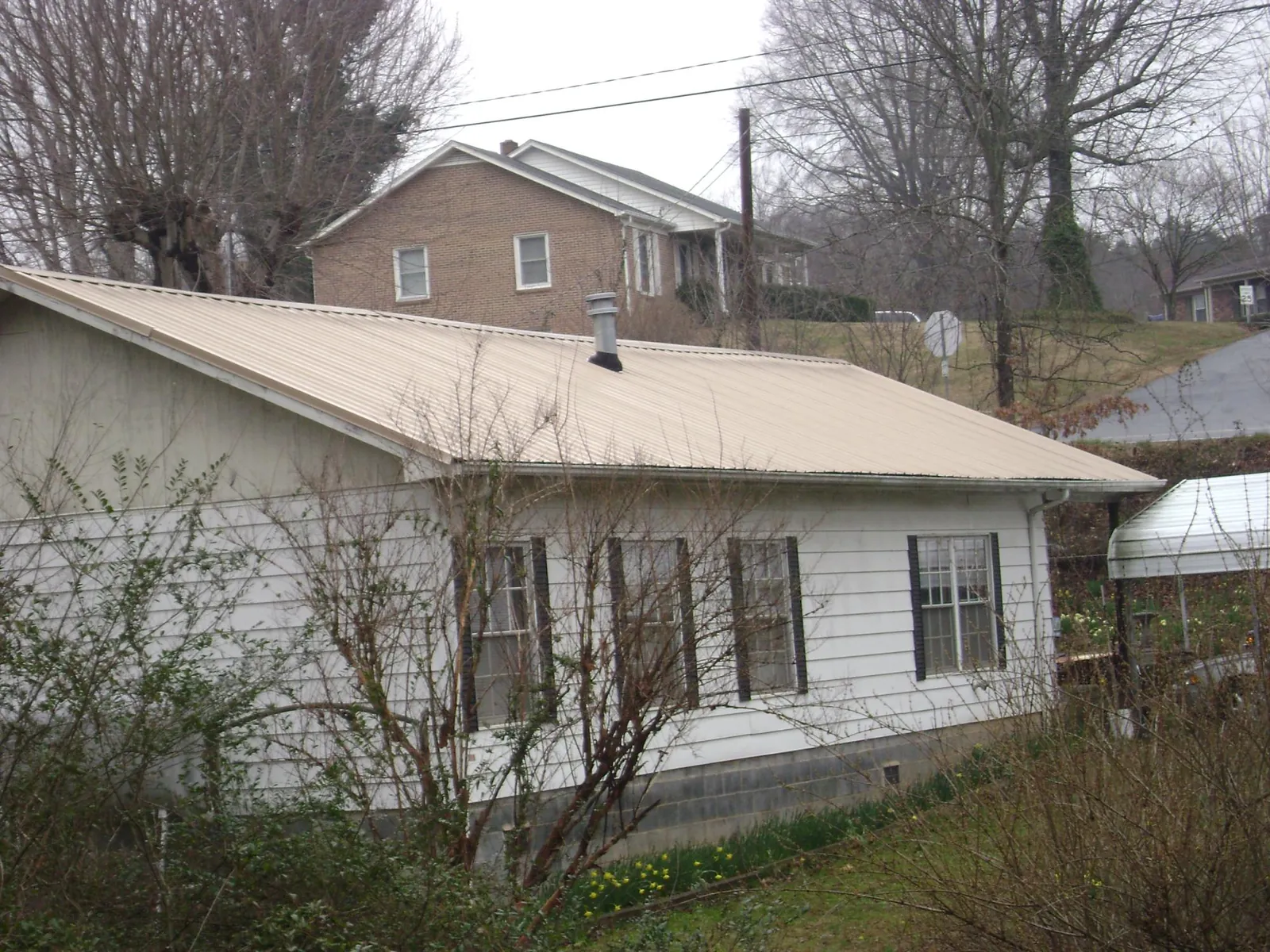 Tan metal roof on a white sided house set into a hillside — Commercial Roofing by Roofing Brothers in Crockett