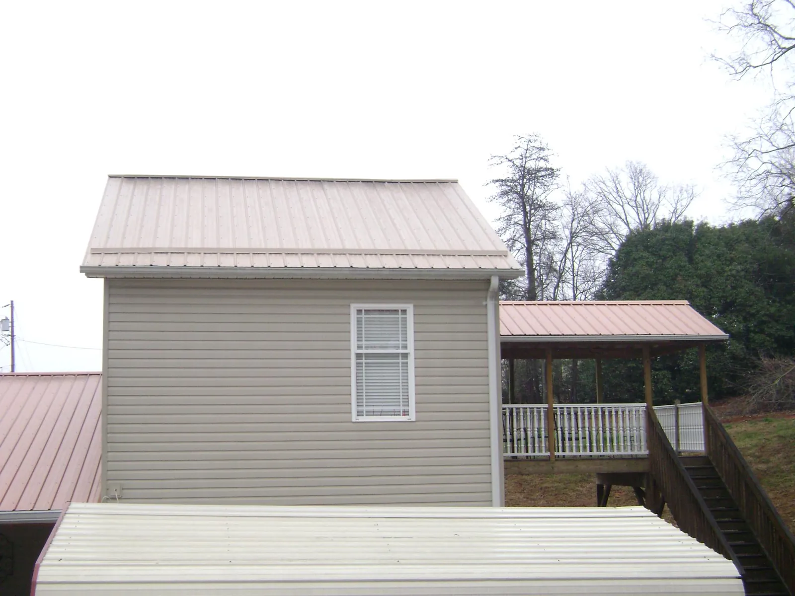 Tan metal roofs on a two story addition and attached porch, from a Roof Replacement job in Crockett